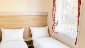 Une chambre avec deux lits, une tête de lit en bois et une fenêtre ornée de rideaux à motifs floraux rouges.