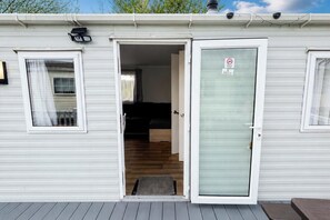 Een stacaravan met een schuifdeur, een klein terras en een zichtbare woonruimte met een bank.