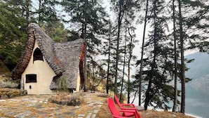 Une petite maison avec un toit à forte pente, entourée d’un chemin de pierre et agrémentée d’une chaise rouge.