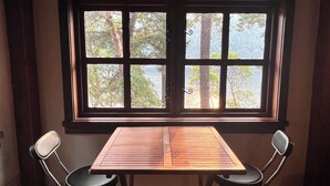 Une pièce avec une table en bois et deux chaises, une fenêtre donnant sur des arbres et une montagne.