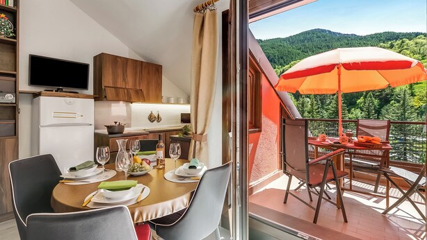 Un coin repas avec une table dressée pour quatre personnes, un téléviseur et un espace cuisine comprenant un réfrigérateur et des placards.