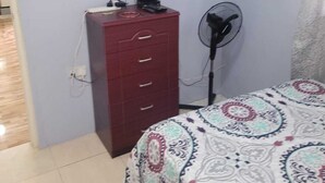 A bedroom with a bed, a TV mounted on the wall, a red dresser, and a standing fan. - J and N Cozy Quarters (Roseau)