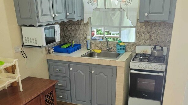 A compact kitchen with grey cabinets, a microwave, a stove, and a sink. - J and N Cozy Quarters (Roseau)
