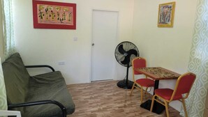 A small room with a sofa, a table with two chairs, a standing fan, and two wall-mounted artworks. - J and N Cozy Quarters (Roseau)