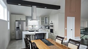 Une cuisine moderne avec des meubles blancs, un îlot central et un coin repas comprenant une table et des chaises en bois.