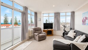 A modern living room with a grey sofa, a recliner, a TV on a wooden stand, and an exercise bike.