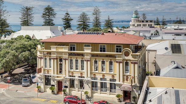 A multi-story building with a red roof, large windows, and a view of the ocean. - Art Deco Escape - Inner City Apartment Napier (Napier)