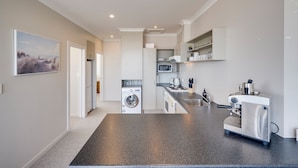 A modern kitchen with a washing machine, microwave, and espresso machine. - Art Deco Escape - Inner City Apartment Napier (Napier)