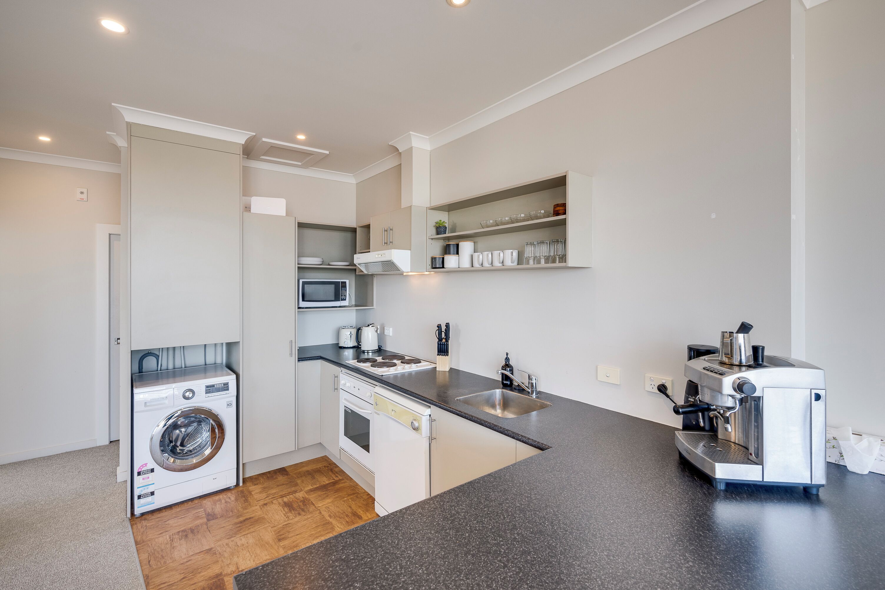 A compact kitchen with a washing machine, oven, microwave, and espresso machine.