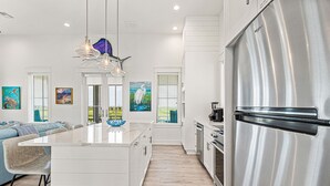 A modern kitchen with a central island, stainless steel appliances, and artwork on the walls. - Modern home w/ two master suites, golf course view - pool, beach, gym, & more (Port Aransas)