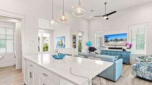 A spacious kitchen with a large island, pendant lights, and a ceiling fan. - Modern home w/ two master suites, golf course view - pool, beach, gym, & more (Port Aransas)