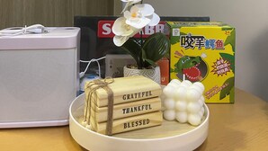 A table with a white speaker, a white orchid, a bowl with wooden blocks, and a box with a cartoon character.