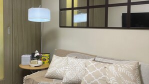 A bedroom with a bed, a bedside table, a lamp, a mirror, and a wardrobe.