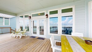 A covered outdoor deck with wooden flooring, white railings, and glass doors leading to a balcony. - Stunning bay front home with fishing pier, large deck, & private pool (Rockport)