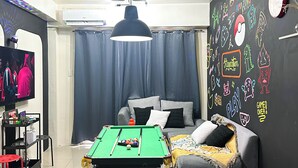 A living room with a pool table, grey sofa, and a wall with colorful doodles. - Granite @ Shore Residences 2BR (Pasay City)