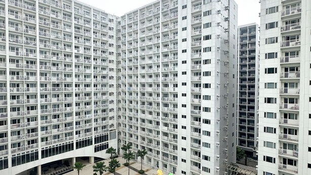 A high-rise residential building with multiple balconies, a central courtyard with palm trees, and a swimming pool. - Granite @ Shore Residences 2BR (Pasay City)