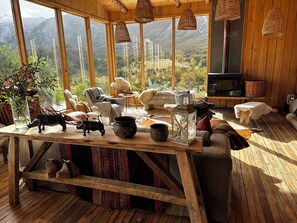 A cozy cabin interior with a large window offering a mountain view, wooden furniture, and rustic decor. - Alto Castillo Lodge  (Rio Ibanez)