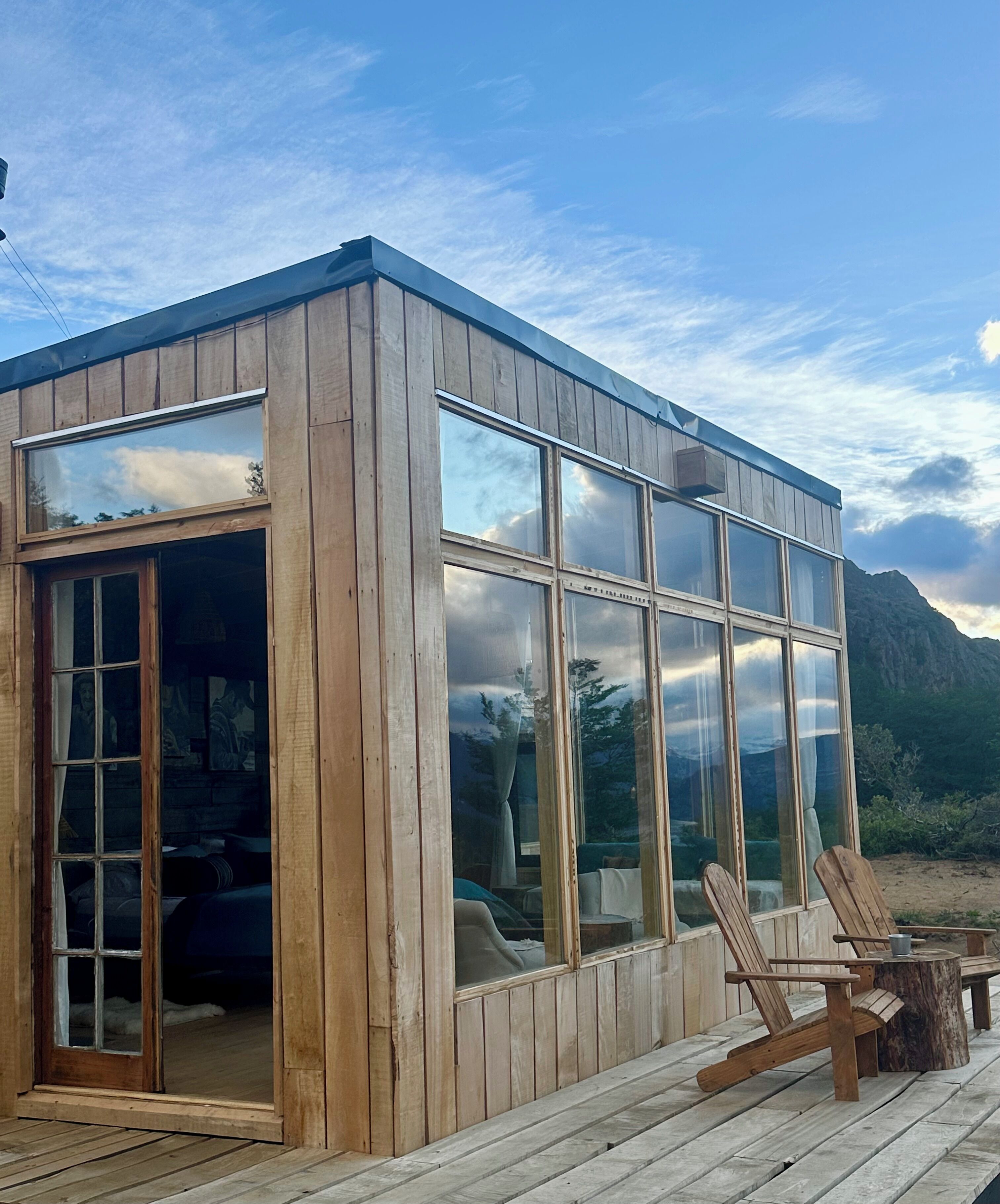 Una cabaña de madera con amplios ventanales, una terraza y mobiliario exterior.