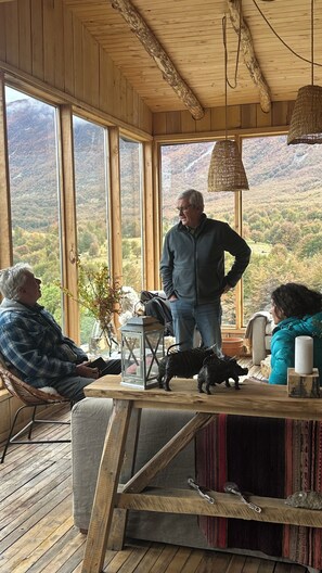 A wooden interior with large windows, a table with figurines, and a mountainous view.