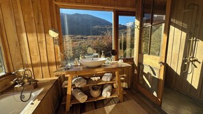 Un baño de cabaña de madera con una ventana grande, un lavamanos, un espejo y una ducha.