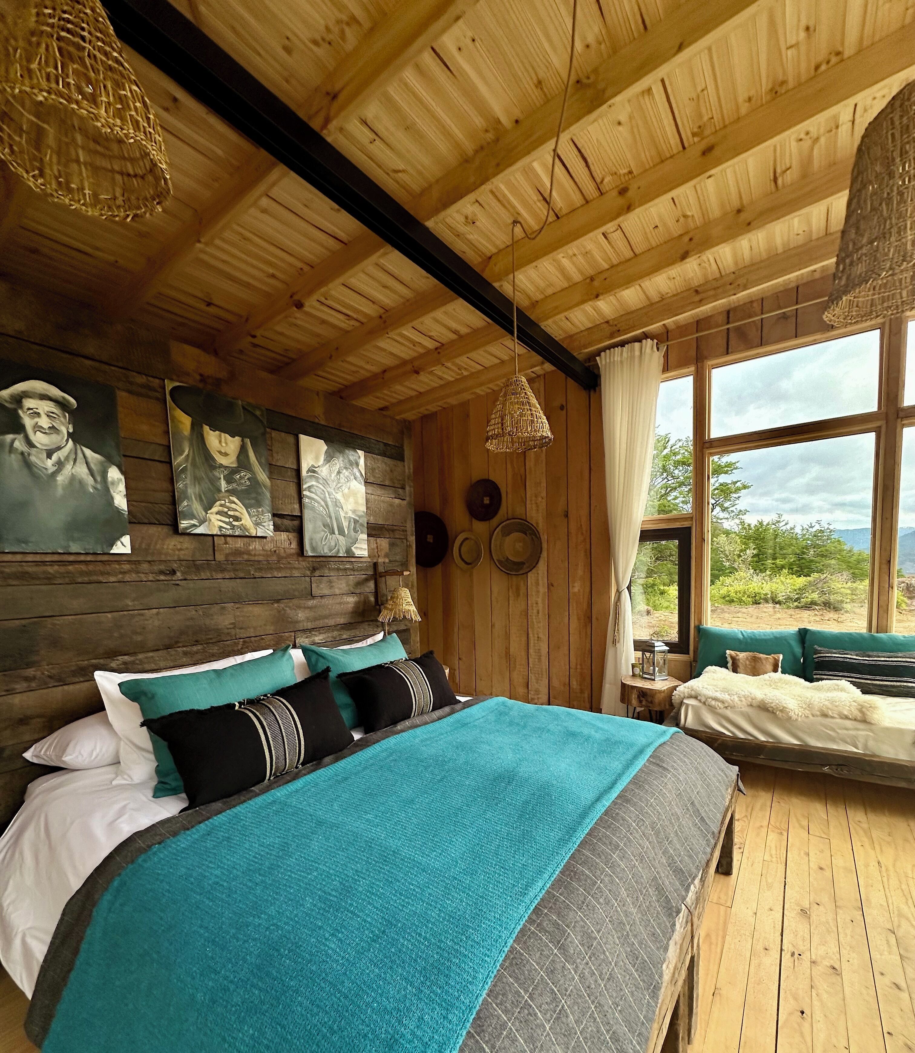 A wooden cabin room with a bed, a window with a view, and wall-mounted artwork.