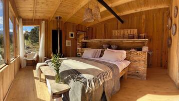 Interno di una baita in legno con un letto, una panca, una finestra vista e un lampadario.