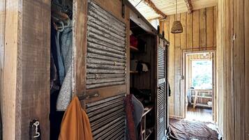 Un intérieur rustique en bois, avec une armoire, des vêtements suspendus et un luminaire tressé.