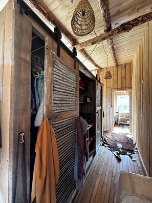 A rustic wooden interior with a wardrobe, hanging clothes, and a woven light fixture. - Alto Castillo Lodge  (Rio Ibanez)