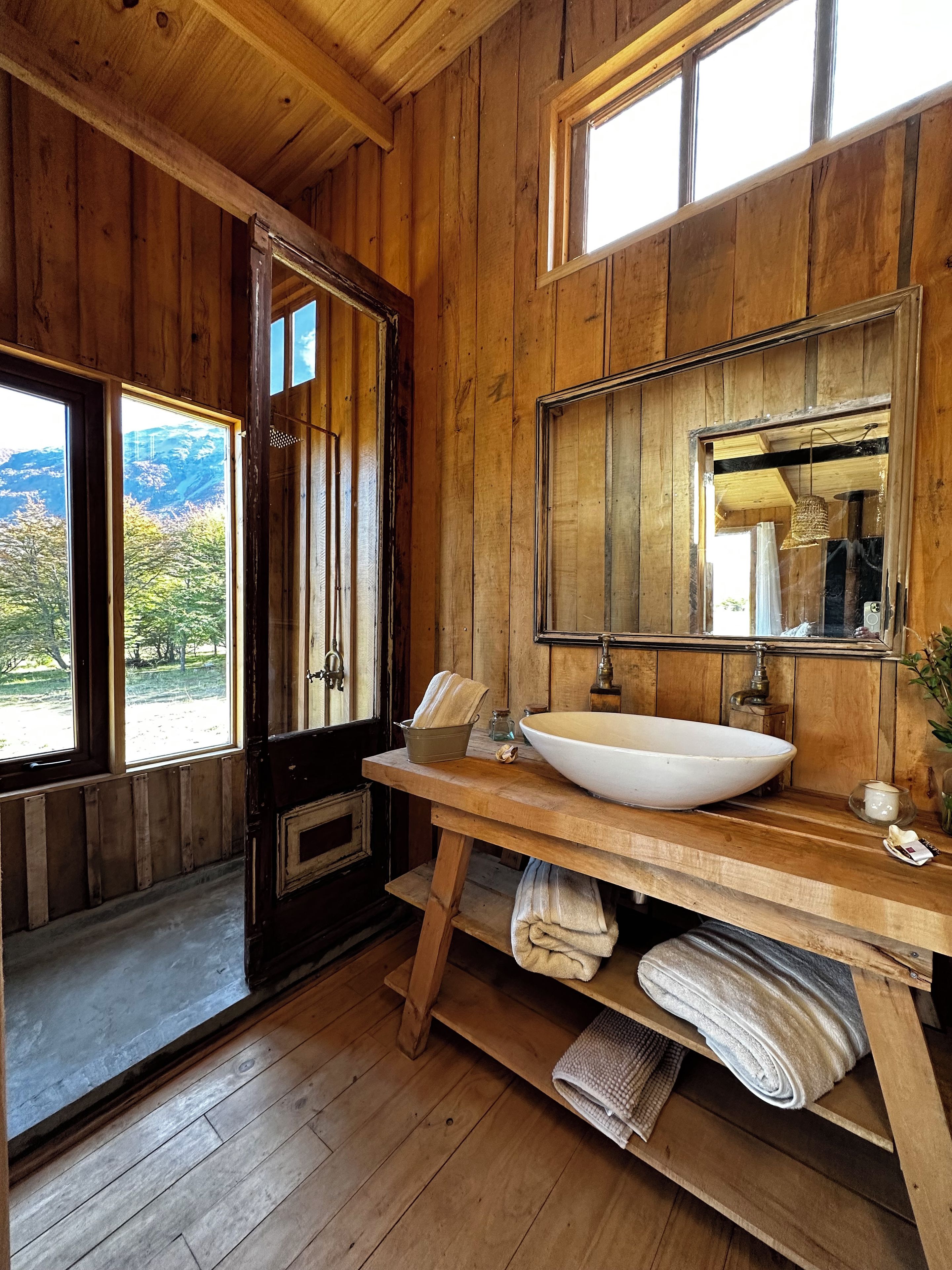 A wooden cabin bathroom with a large window, wooden vanity, and a sink.