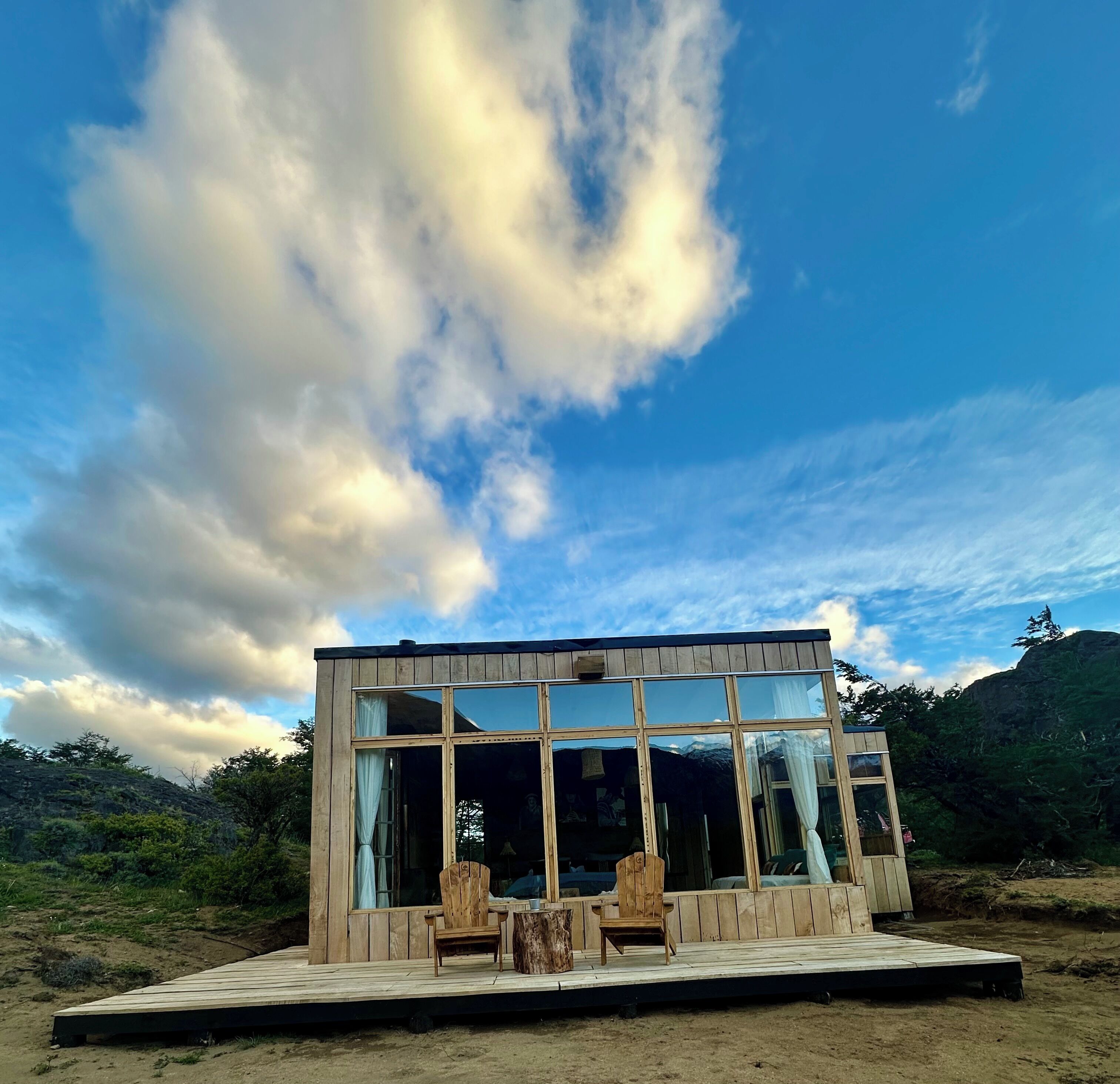 Una cabaña moderna de madera con ventanas amplias, una terraza y una silla.