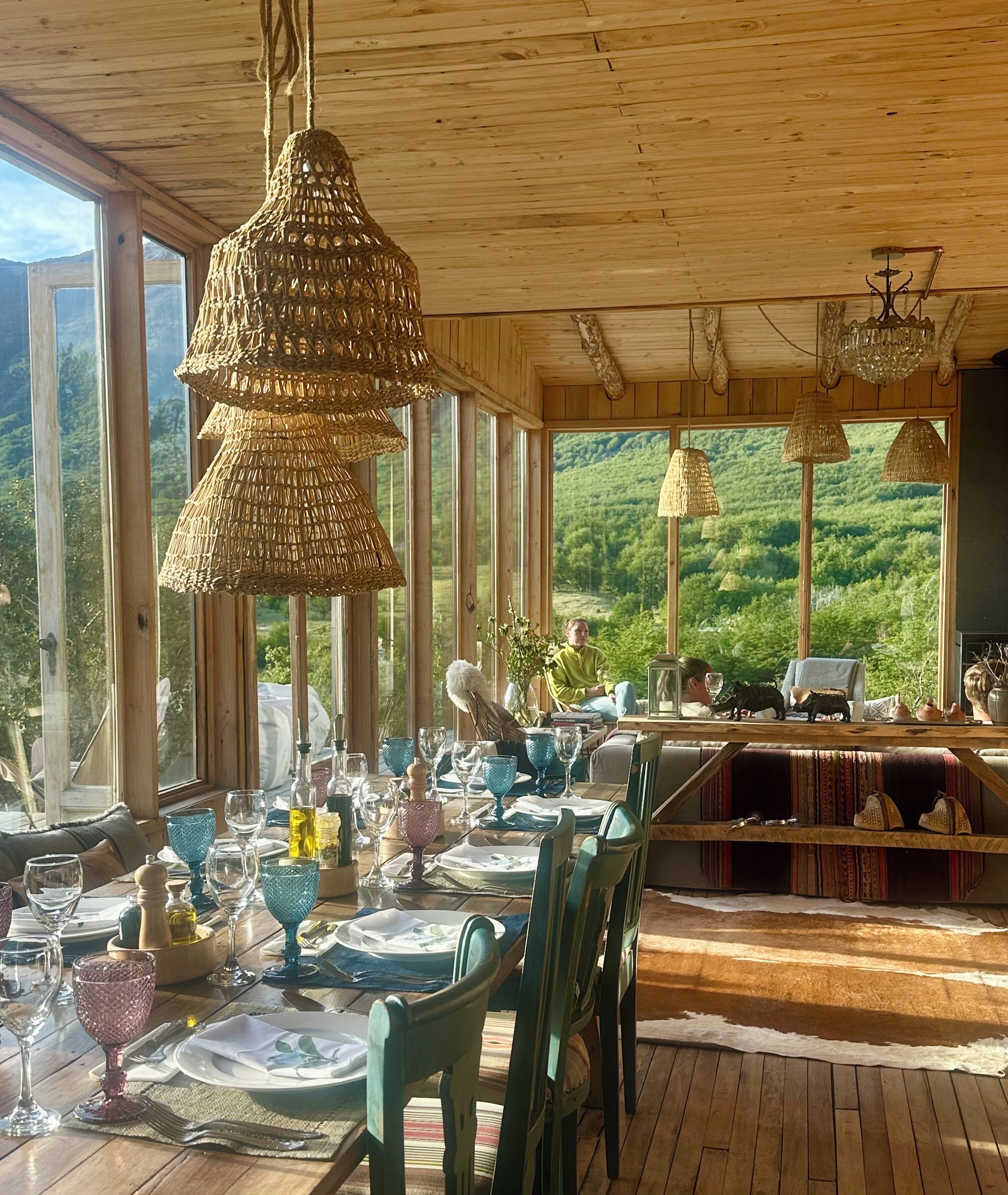 A dining area with a table set for four, large windows, and a view of a forested landscape.