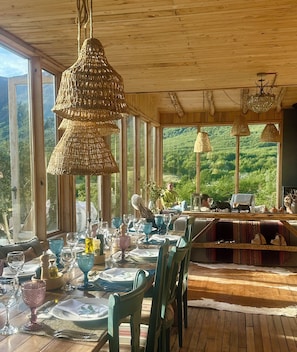 Comedor con una mesa preparada para cuatro, ventanas amplias y vistas a un paisaje boscoso.