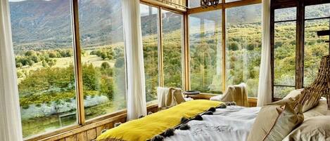 A bedroom with a large bed, multiple windows, and a view of a mountainous landscape.