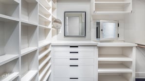 A white closet with multiple shelves and drawers, a mirror, and a frosted glass door. - Stunning Home in South Highland (Shreveport)