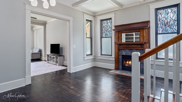 A spacious living room with hardwood flooring, a fireplace, and large windows with stained glass. - Stunning Home in South Highland (Shreveport)