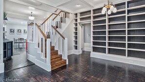 A spacious interior with a wooden staircase, white walls, and a large built-in shelving unit. - Stunning Home in South Highland (Shreveport)