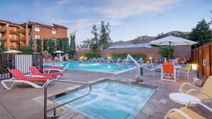 A rooftop pool area with lounge chairs, a hot tub, and a view of a mountain.