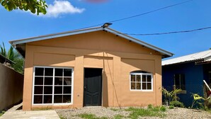 A single-story house with a beige exterior, a front door, two large windows, and a small porch area. - JOY & PEACE HOUSE come to enjoy our brand new house . (Tela)