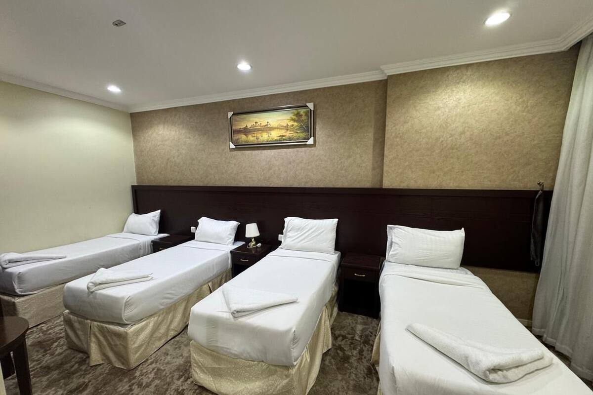 Ein Hotelzimmer mit drei Einzelbetten, einem Kopfteil, einem Gemälde an der Wand und einem Teppichboden.