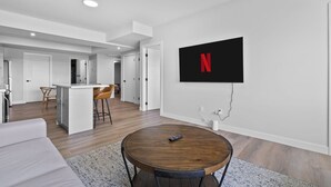 Una sala de estar moderna con una mesa de centro redonda de madera, un sofá blanco y una zona de cocina al fondo.