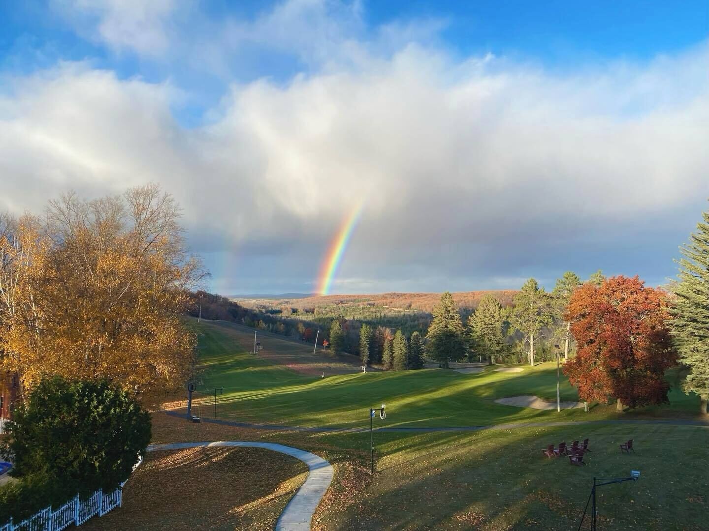 Un campo de golf con un arcoíris, árboles y cielo despejado.