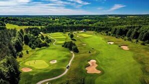 Um campo de golfe com vários buracos, rodeado por florestas densas e um céu limpo.