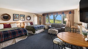 Quarto de hotel com duas camas, uma mesa de jantar, um sofá e uma televisão.