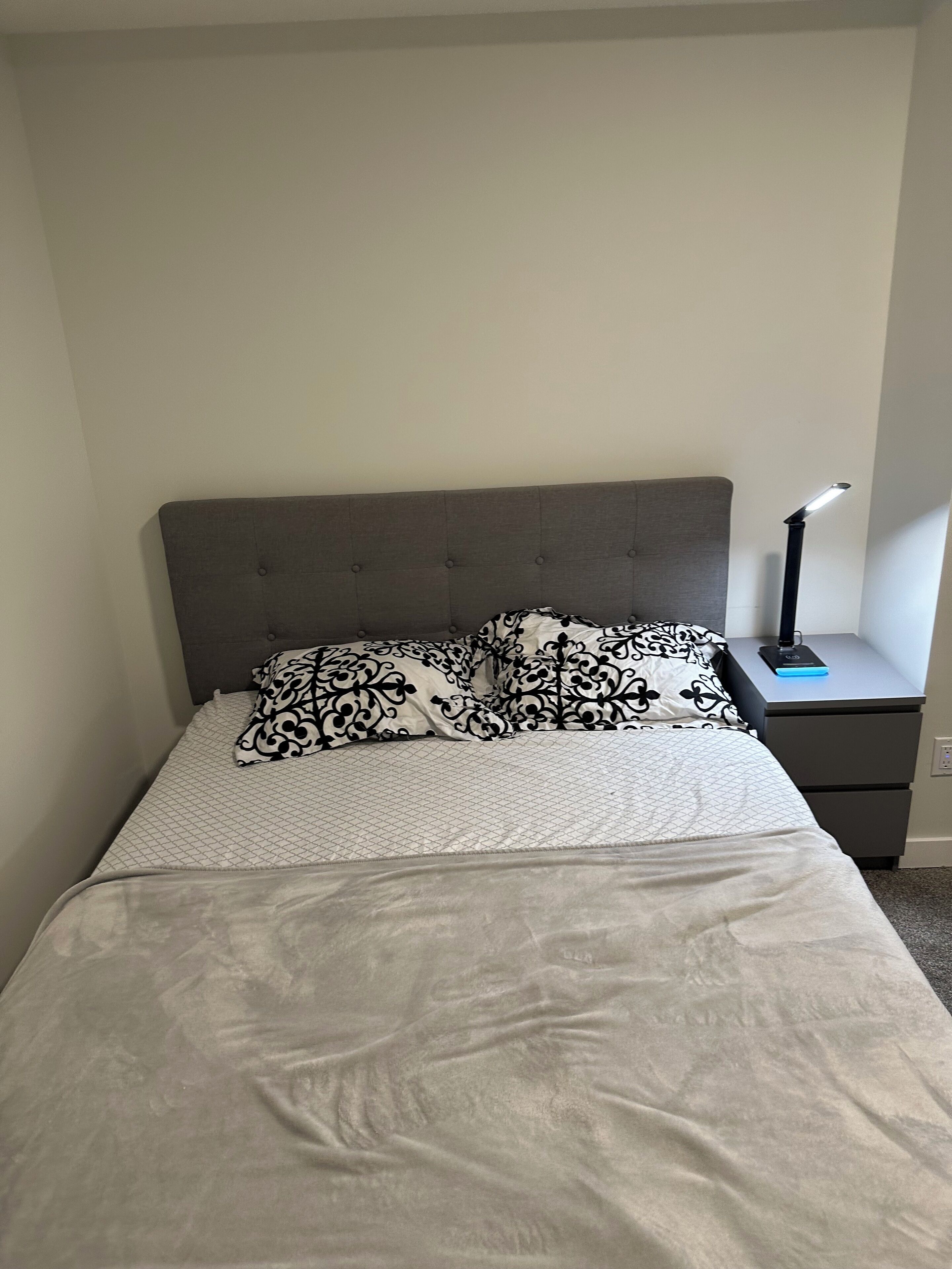 A neatly made bed with a grey headboard, a patterned pillow, and a bedside table with a lamp.