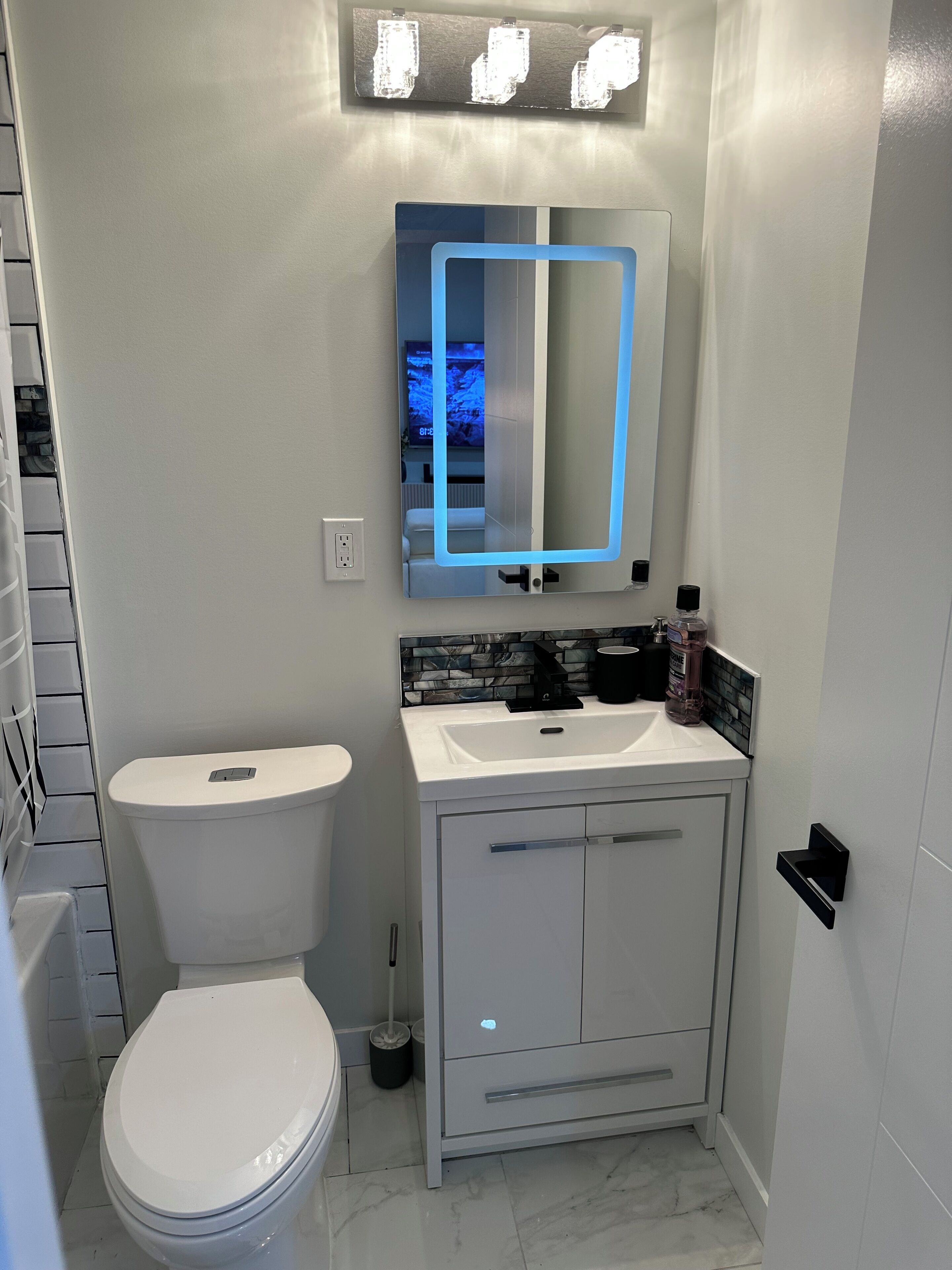 A modern bathroom with a white toilet, a sink with a mirror above it, and a cabinet below.