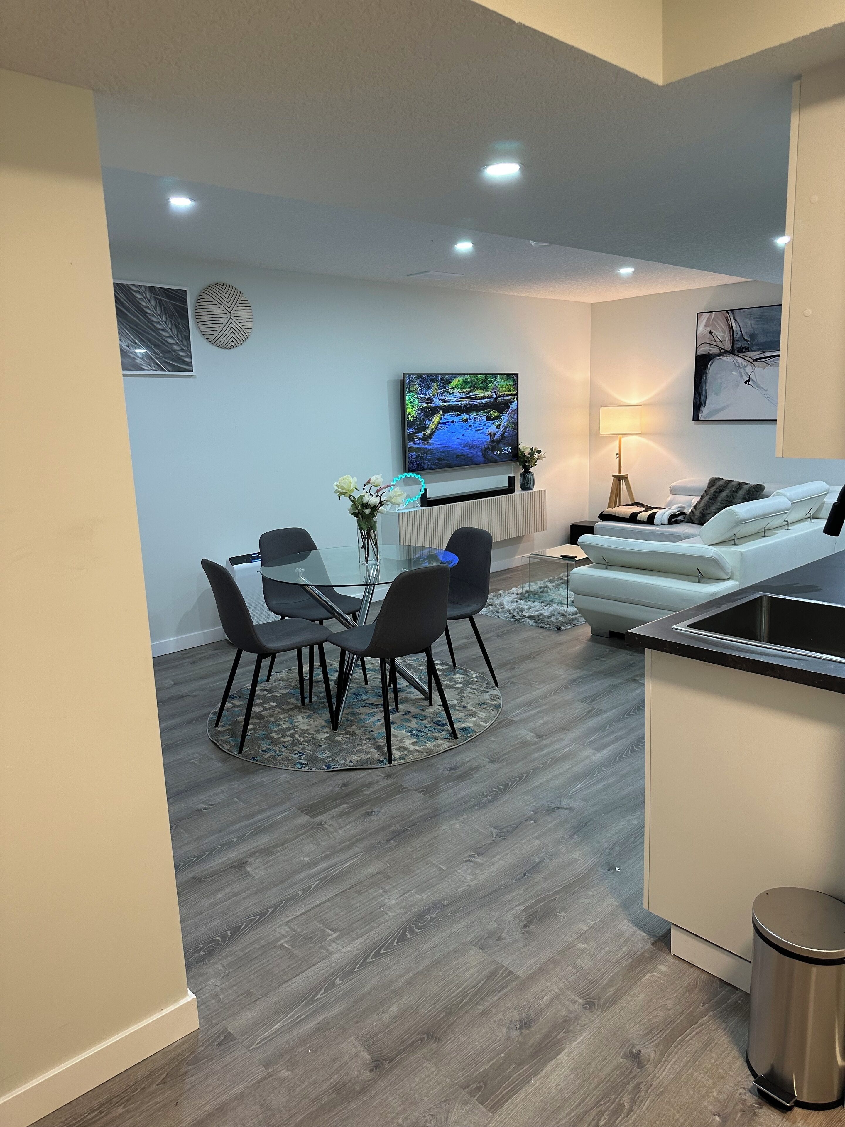 A modern living room with a dining area, a TV mounted on the wall, a sofa, and a small kitchen area.