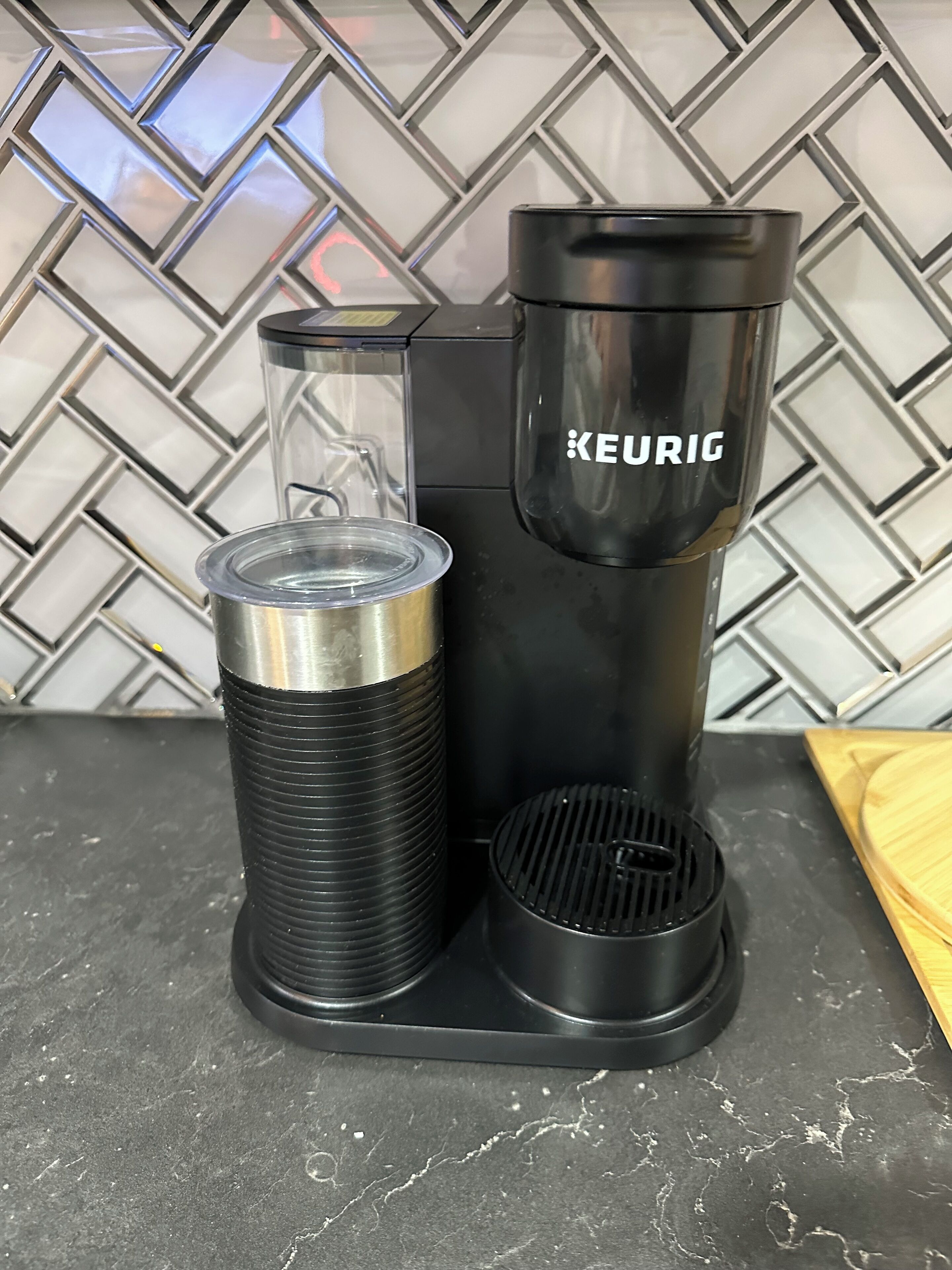 A Keurig coffee maker with a transparent water reservoir and a black drip tray on a kitchen counter.