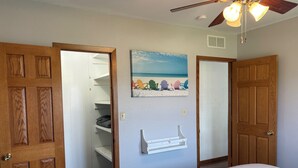 A bedroom with a bed, a ceiling fan, a closet with shelves, and a beach-themed painting on the wall. - Popular Rathbun Lake Getaway (Mystic)