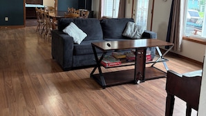A spacious living room with a dark-colored sofa, a coffee table, and a dining area in the background. - Popular Rathbun Lake Getaway (Mystic)
