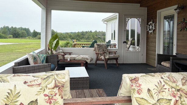 A covered porch with wicker furniture, a ceiling fan, and a view of a green landscape. - Popular Rathbun Lake Getaway (Mystic)
